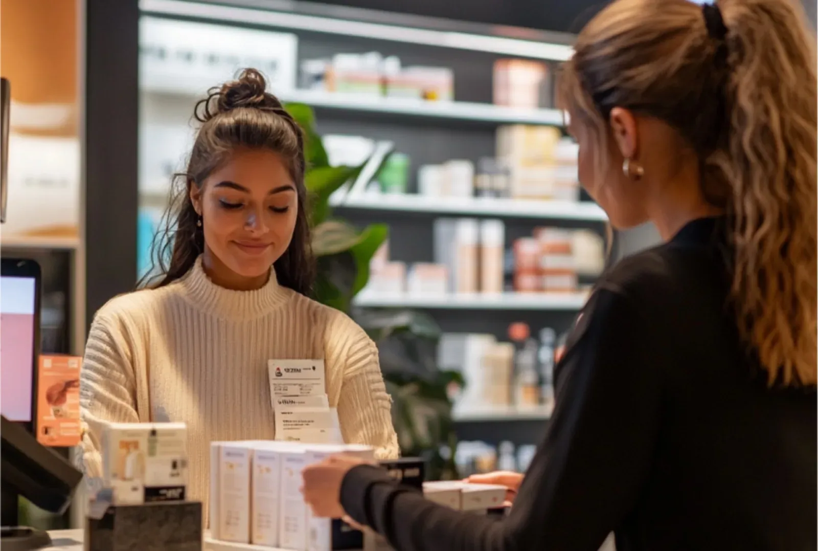 Una dependienta está atendiendo a una clienta en una tienda de cosméticos, entregándole varios productos mientras le muestra una factura. El ambiente es moderno, con estantes llenos de artículos de belleza al fondo.